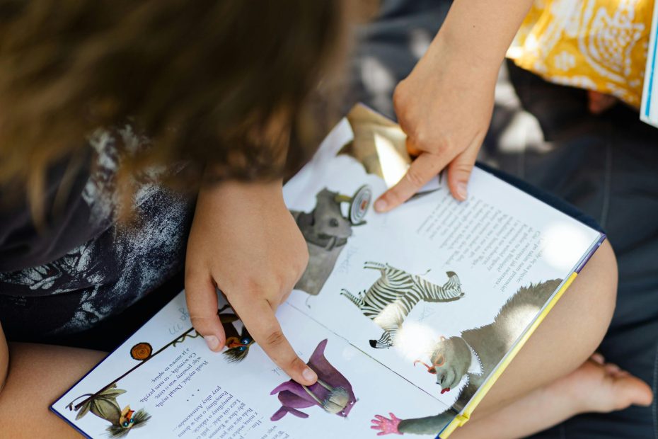 Looking down at a book in a child's lap. The child is pointing at a purple walrus drawing.