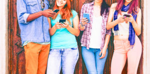 Group of teenagers texting  mobile phone messages leaning against urban  wall - Row of best student friends using smartphone wearing summer trendy clothing.