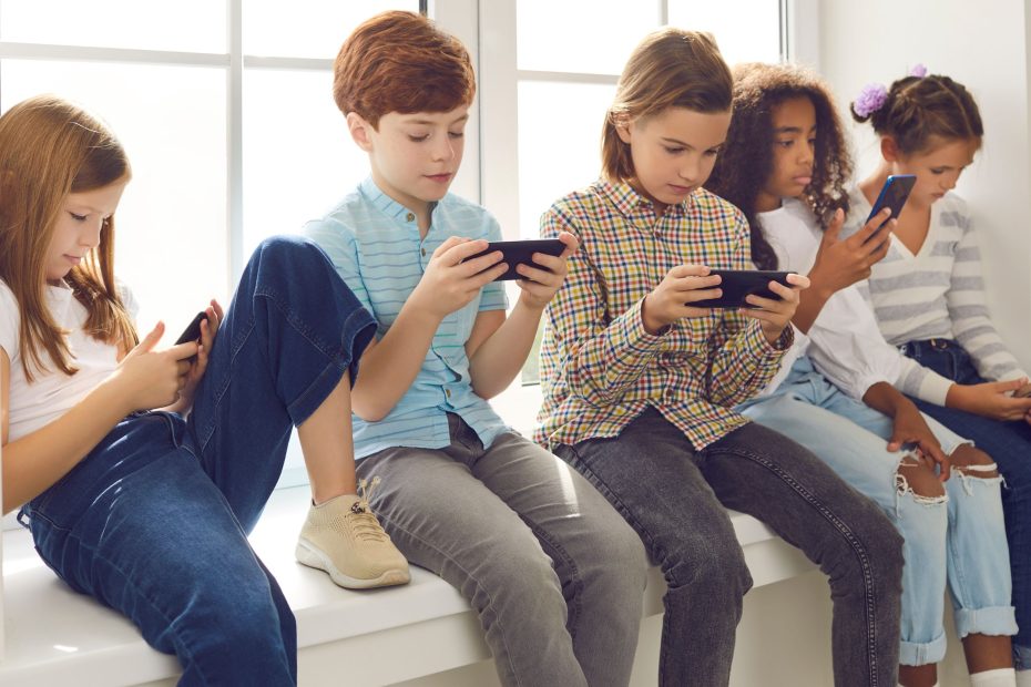 Group of teenagers texting mobile phone messages leaning against urban wall - Row of best student friends using smartphone wearing summer trendy clothing.