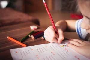 Child writing a note with a red pencil.