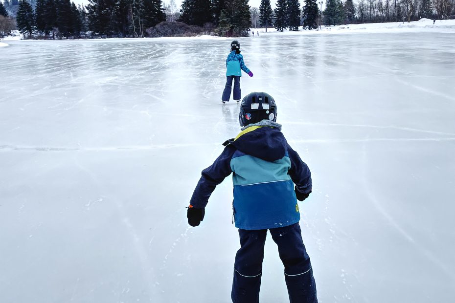 Two kids ice skating on the pond in Hawrelak Park, Edmonton.