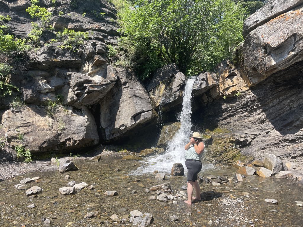 Woman taking a photo of the photographer with Rainbow Falls at the end of Miner's Path in the background.
