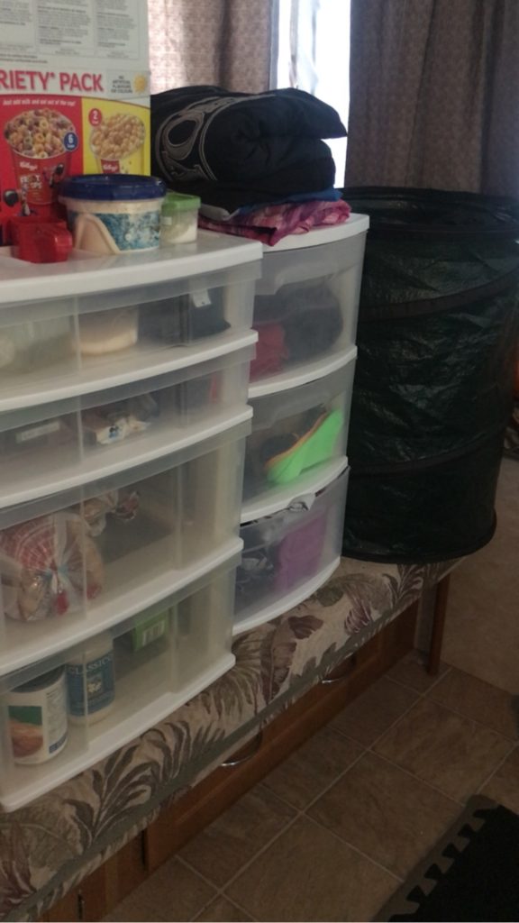 Sterilite bins used to hold food and clothes while camping set up on the bench in a tent trailer.