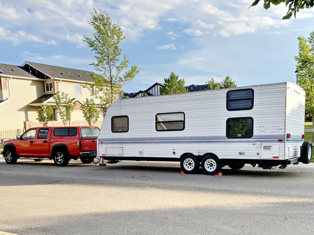 Orange truck parked in front of a late-90s trailer on a residential street.